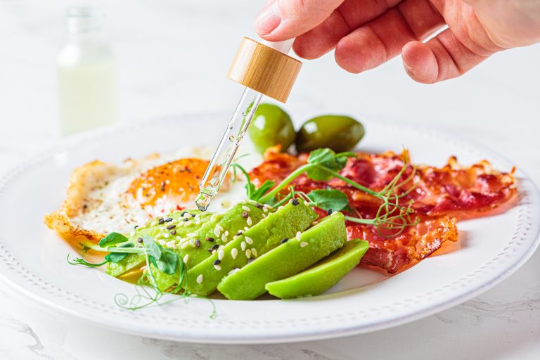 Fried egg with avocado and fried bacon in white plate.
